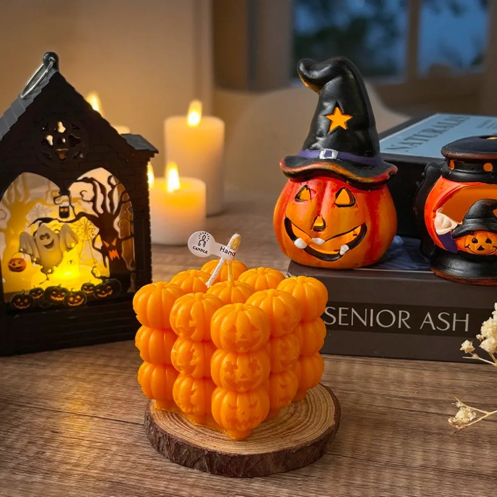 An orange silicone pumpkin mold is displayed next to a witch hat decoration and candles on a wooden surface.