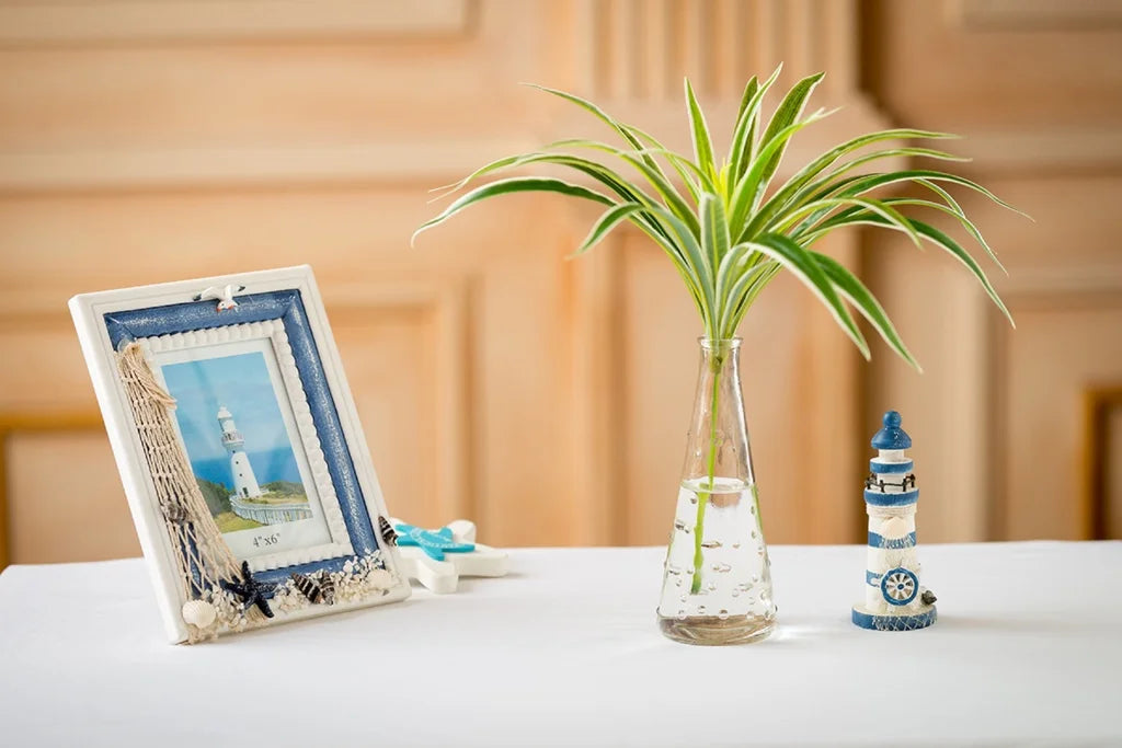 A tall glass vase holds a vibrant green artificial chlorophytum branch on a white table.