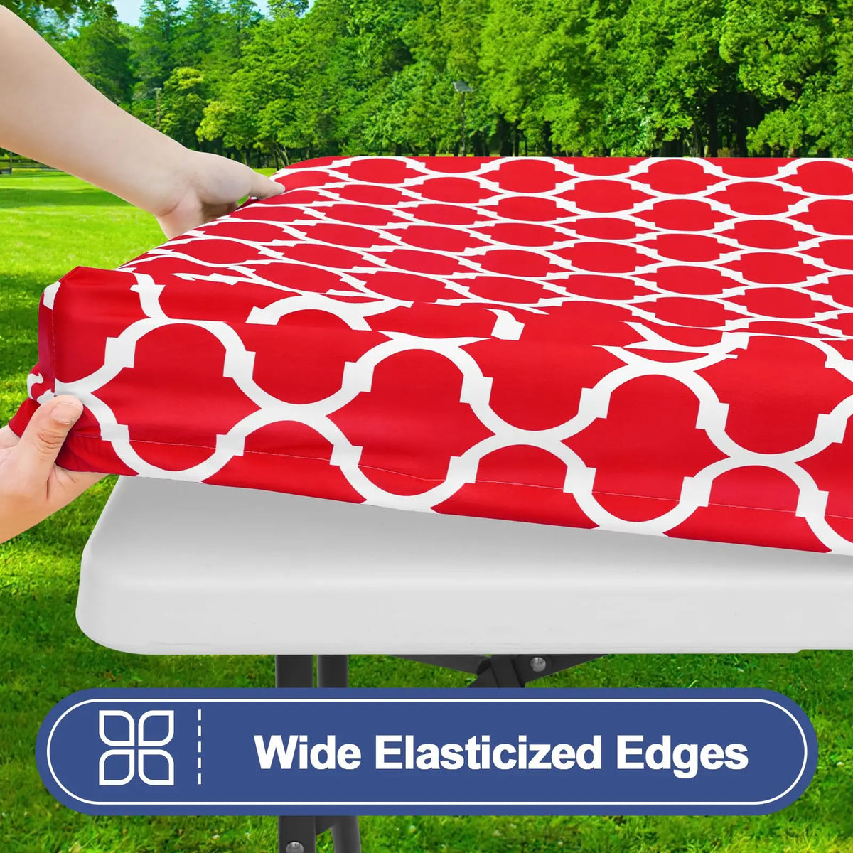 A red patterned waterproof elastic fitted tablecloth is being held over a white table surface outdoors.