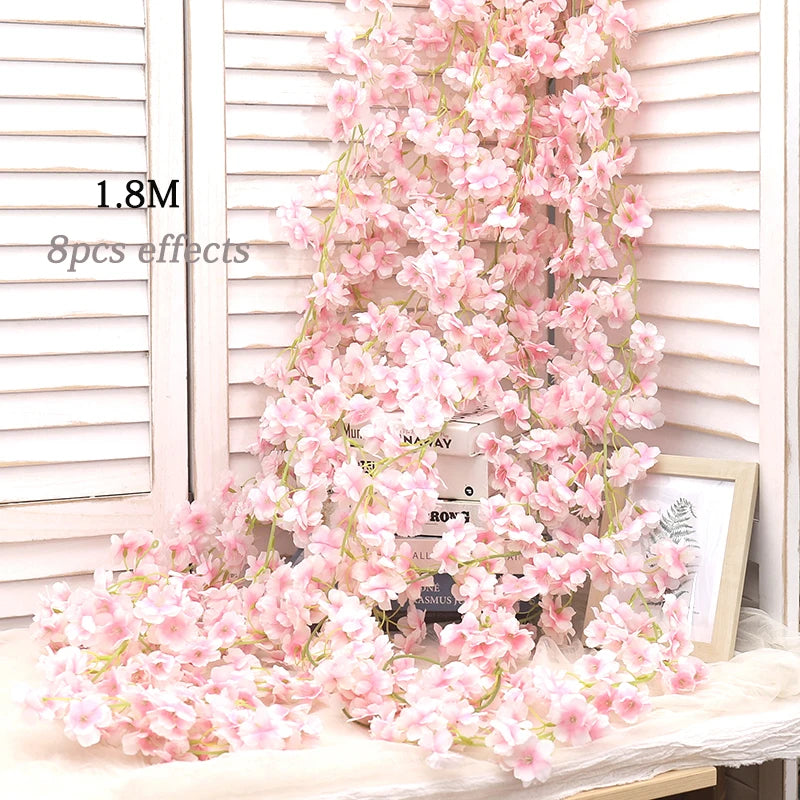 A long garland of pink artificial sakura flowers draped against a white wooden background.