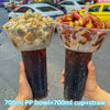 A hand holds a tall plastic cup filled with a dark beverage and straw, next to another similar drink.