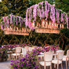 An outdoor event decorated with hanging floral chandeliers made of artificial wisteria vine garlands and purple flowers.