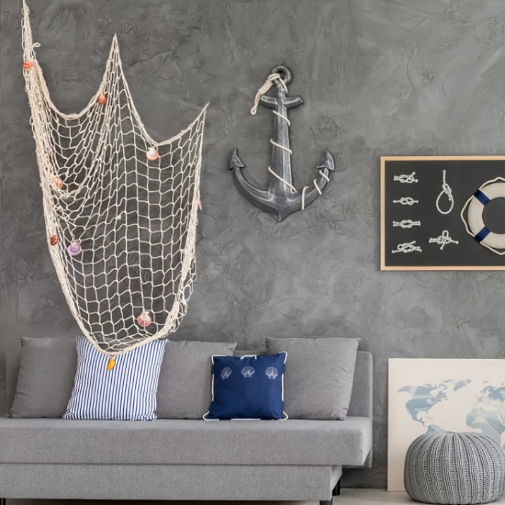 Una pared gris con un ornamento de red de pesca y un ancla colgada sobre un sofá gris.