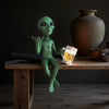 A resin statue of a green alien holding a beer glass on a wooden table.