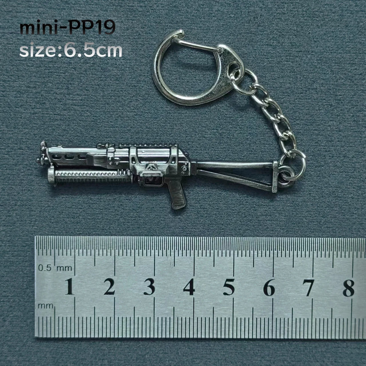 A silver alloy gun model miniature keychain with a chain and jump ring, shown next to a ruler.