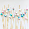 A collection of pearl-tipped bamboo cocktail picks with a white pearl finish arranged diagonally on a white background.