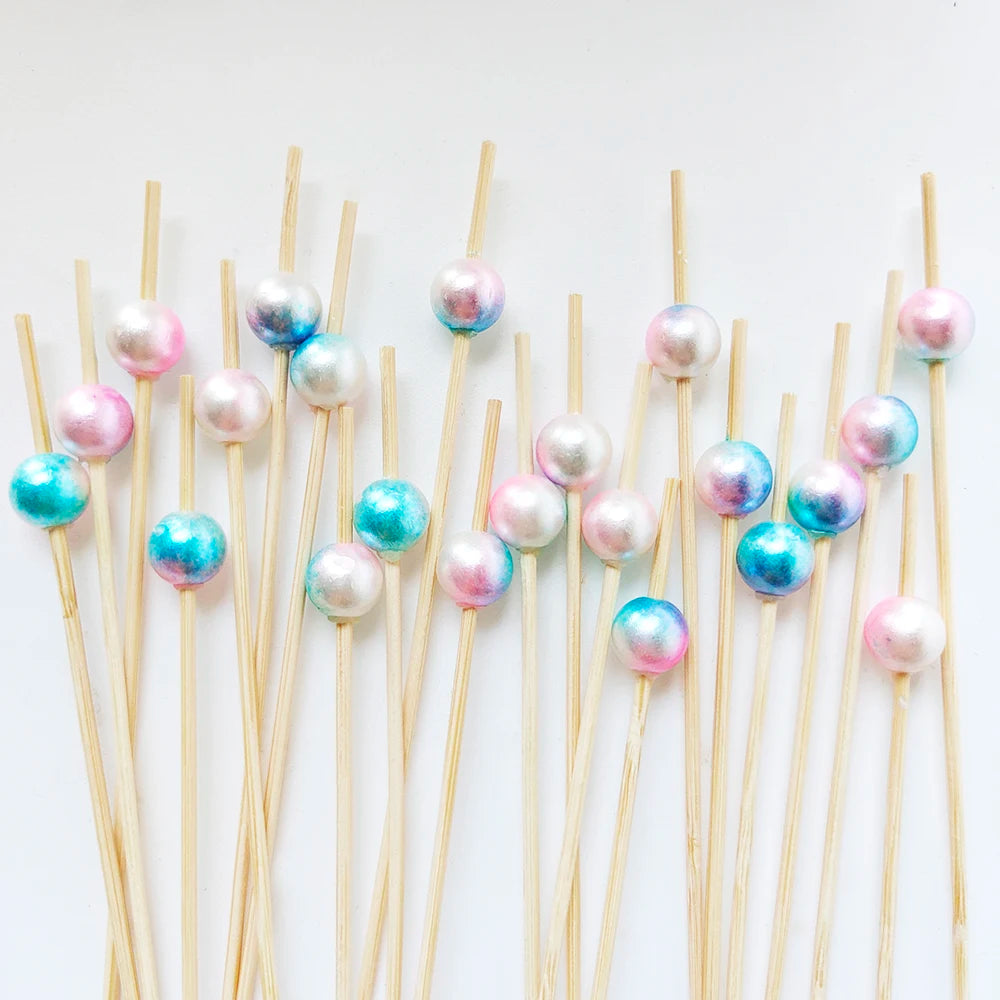 A collection of pearl-tipped bamboo cocktail picks with a white pearl finish arranged diagonally on a white background.