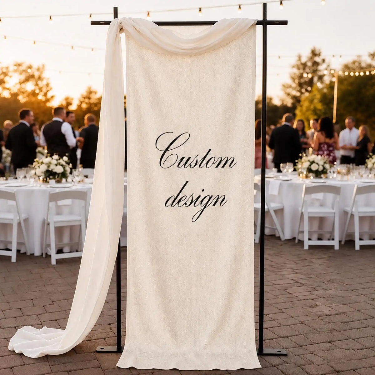 A cream linen banner with custom design text hangs from a black stand outdoors for an event.