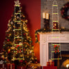 A decorated Christmas tree with a vertical light ladder and Santa figures next to a fireplace