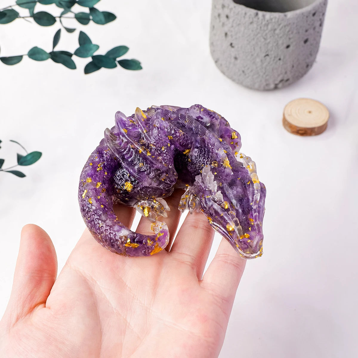 A hand holds a purple crystal dragon figurine with gold inclusions on a white background.