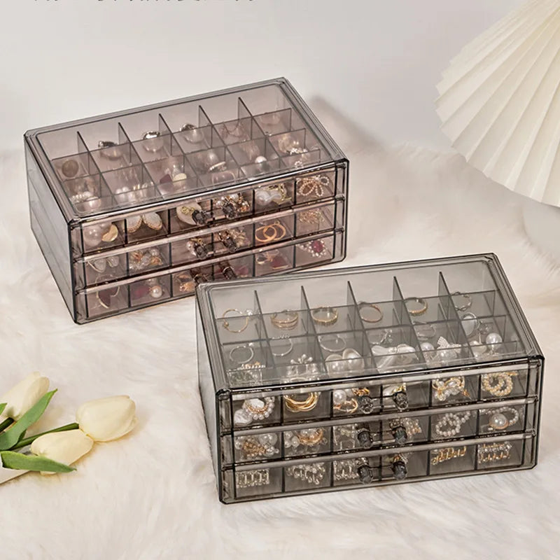 Clear acrylic jewelry organizer with three drawers displaying various rings and earrings.