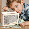 A young boy is looking at a wooden money saving box with a built-in goal tracker and stacks of paper money.