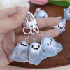 A hand holds a set of glow-in-the-dark ghost keychains with white clasps and silver rings.