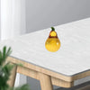 A yellow crystal glass pear figurine is displayed on a white table surface.