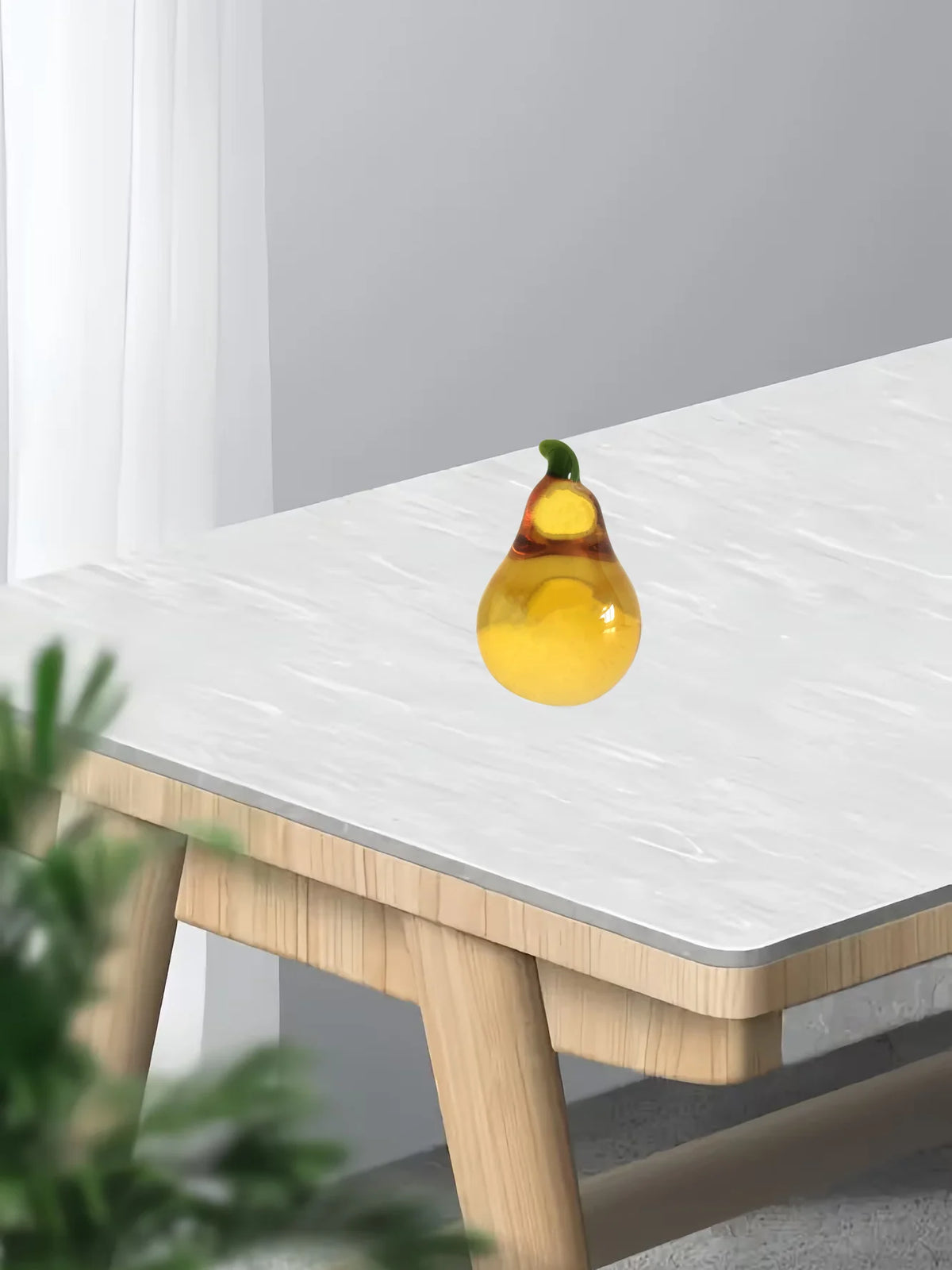 A yellow crystal glass pear figurine is displayed on a white table surface.