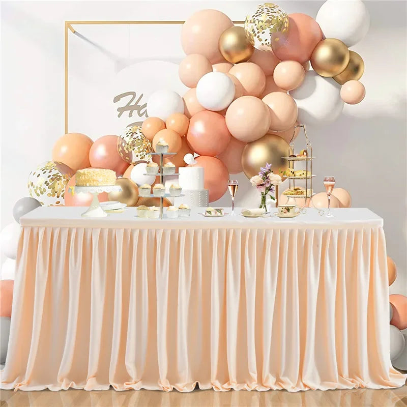 A round table draped with a peach pleated polyester skirt, surrounded by a large balloon arrangement.