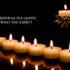 A row of glowing beeswax tealight candles casting warm light on a reflective surface.