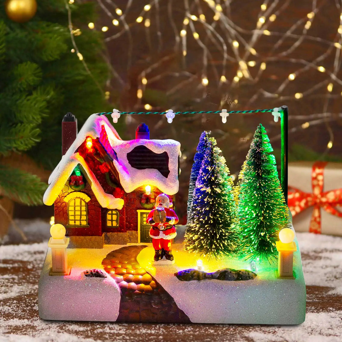 Illuminated Christmas village scene featuring a red house, Santa, and glowing green and blue snowy trees.