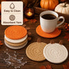 A set of four crocheted pumpkin coasters in various shades of orange and cream resting on a wooden surface.