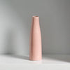A tall, smooth, pink ceramic vase standing on a white shelf.
