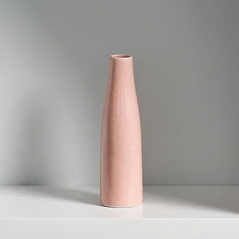 A tall, smooth, pink ceramic vase standing on a white shelf.
