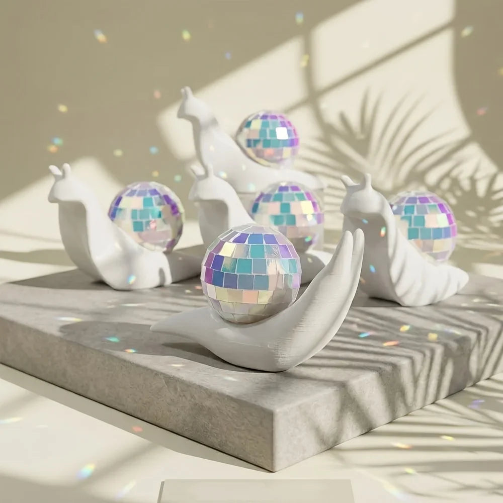 White snail figurines with iridescent disco balls are displayed on a gray surface.