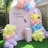 A display of pastel rainbow latex balloons in pink, purple, yellow, and blue arranged in an arched backdrop.