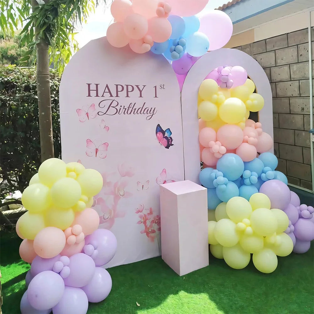 A display of pastel rainbow latex balloons in pink, purple, yellow, and blue arranged in an arched backdrop.