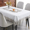 White embroidered lace tablecloth set for a dining table with modern chairs and wooden cabinet in the background