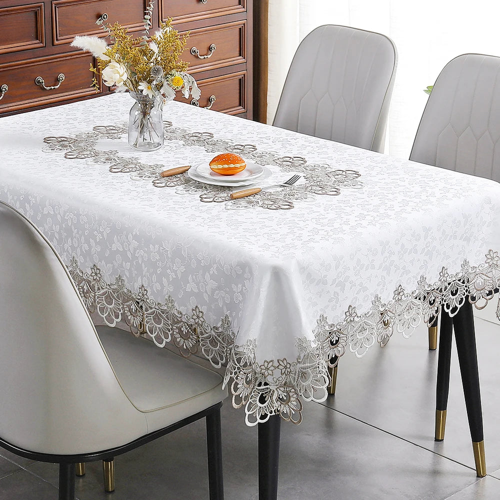 White embroidered lace tablecloth set for a dining table with modern chairs and wooden cabinet in the background