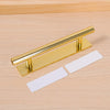 Gold self-adhesive cabinet handles for drawers and wardrobes, shown against a light wood background.