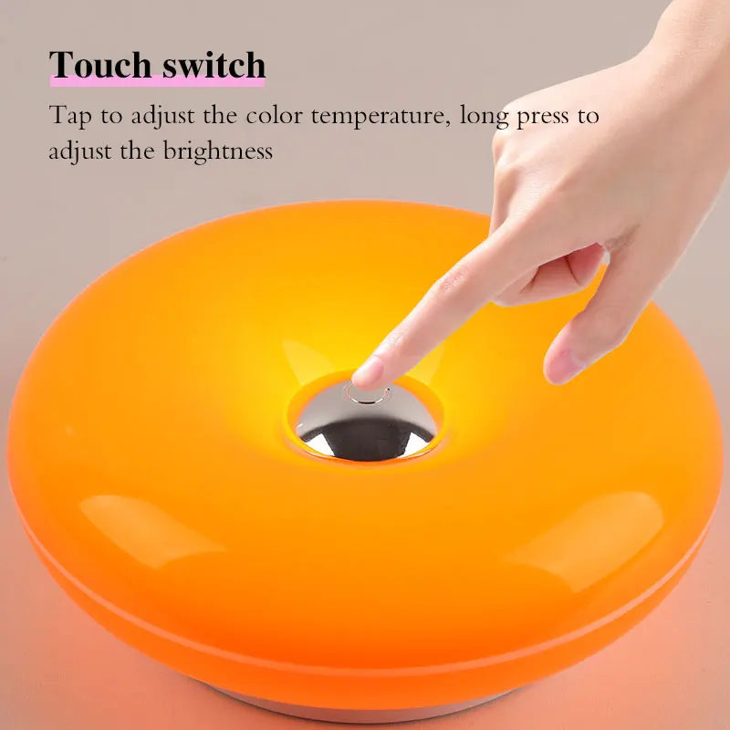 Hand justiert die Helligkeit einer orangen, donutförmigen, wiederaufladbaren Wandlampe mit einem Touchschalter.