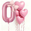Pink foil balloons shaped like the number zero and hearts with pink bows for party decoration