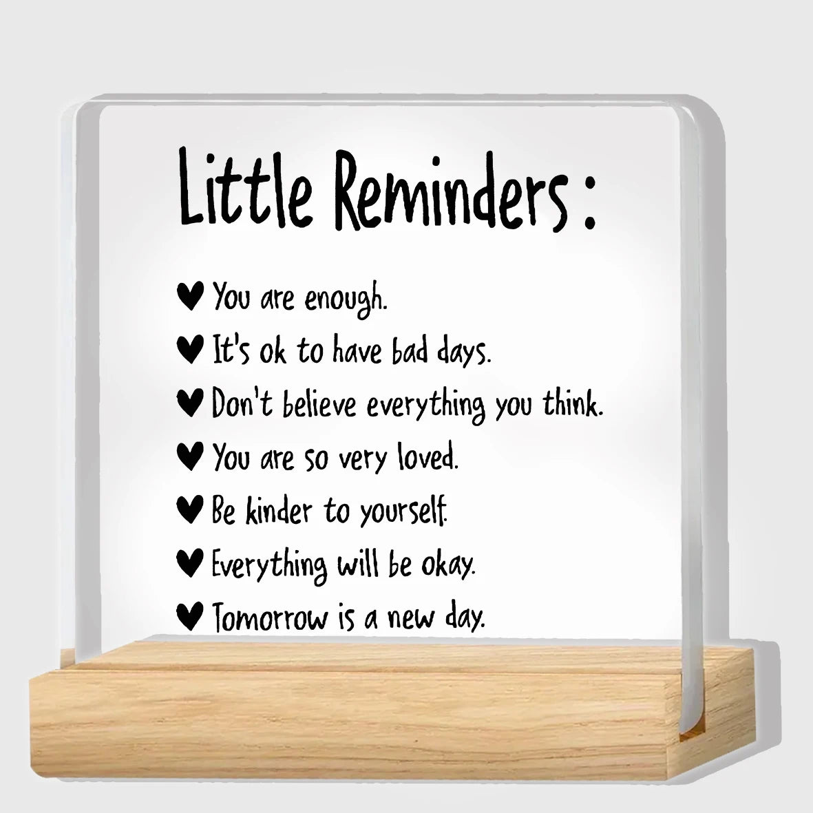 A clear acrylic desk plaque with black text listing little reminders such as You are enough and Everything will be okay.