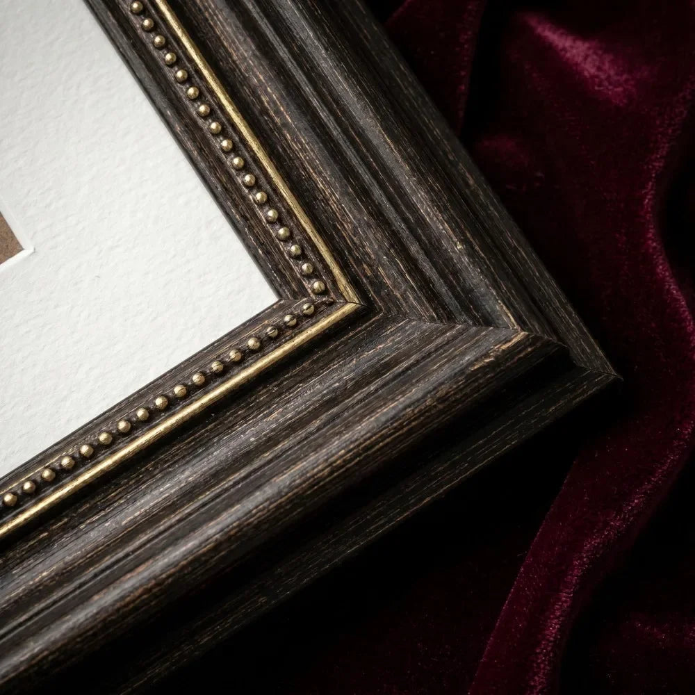 A dark wood photo frame with antique gold trim resting on a deep burgundy velvet fabric.