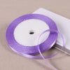 Purple satin ribbon spool with a white core lying on a white surface.