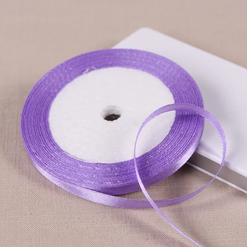 Purple satin ribbon spool with a white core lying on a white surface.