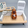 Pendentif de capybara orange avec détail blanc sur une étagère en bois près d'un appareil électronique blanc.