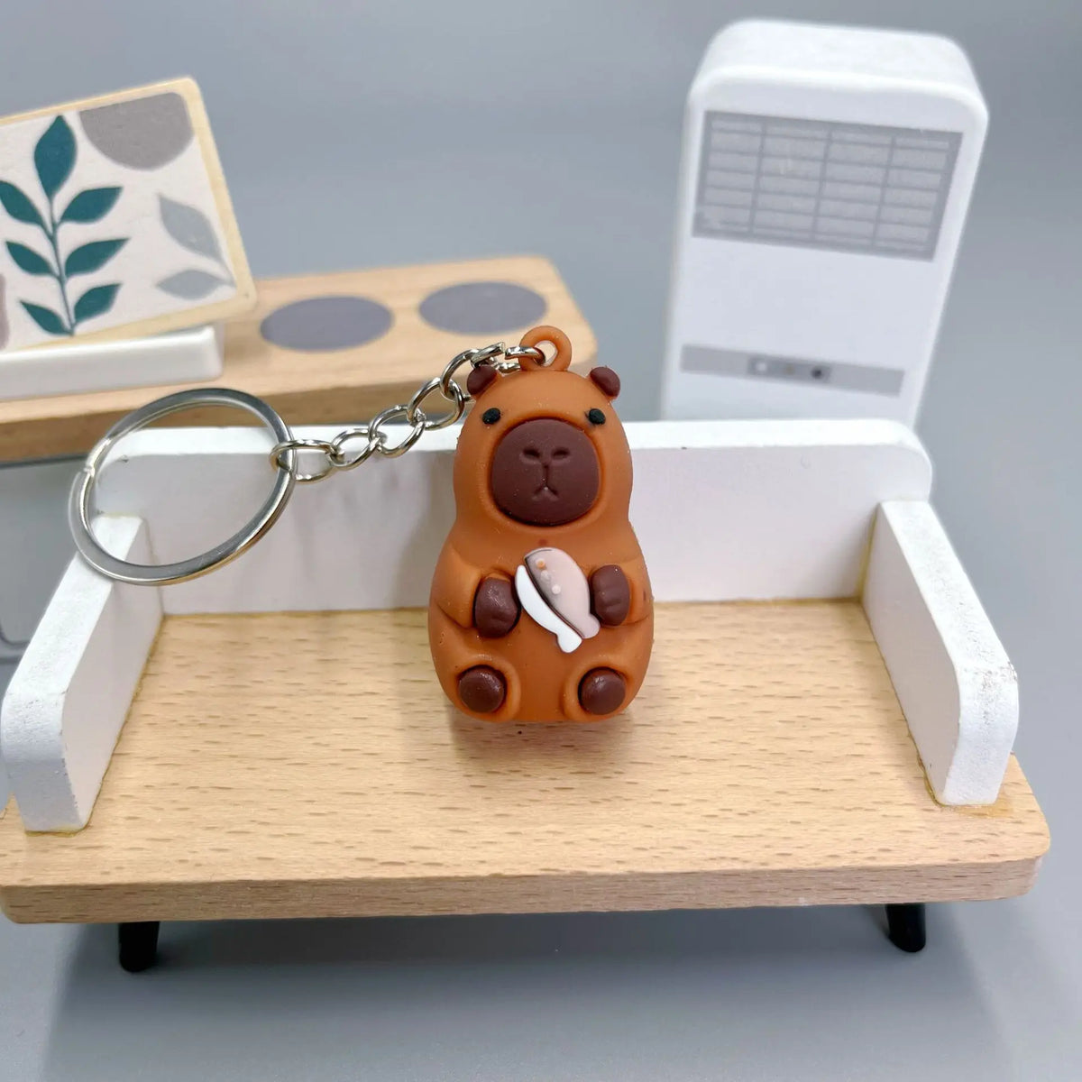 Pendentif de capybara orange avec détail blanc sur une étagère en bois près d'un appareil électronique blanc.
