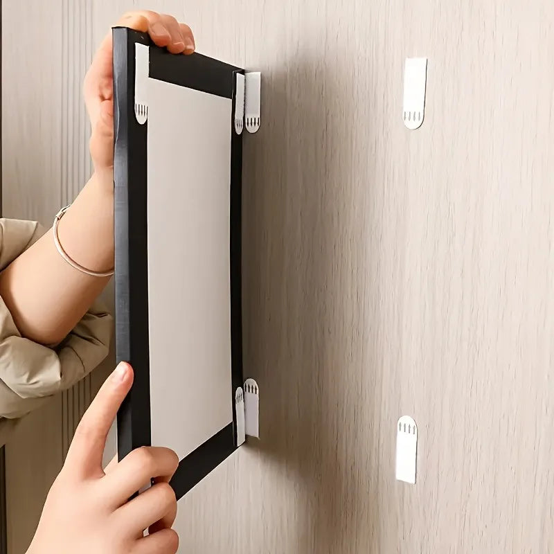 Manos instalando tiras de colgado para cuadros resistentes en una pared de color claro.