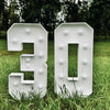 A white marquee number sign displaying the number 30 is placed in tall green grass outdoors.