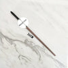 A long, slender metal wand replica with a circular metal core is displayed on a white marble surface.