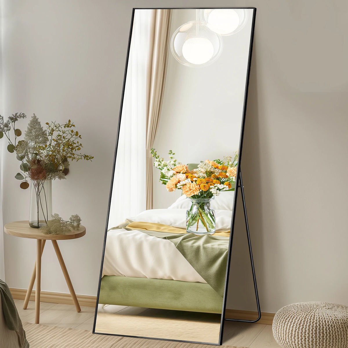 A full length arched wall mirror reflects a bedroom with white bedding and orange floral arrangements.