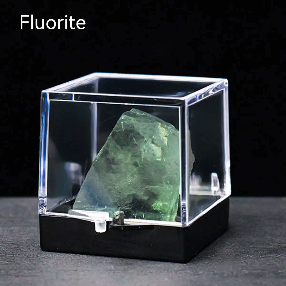 A clear glass box displays a green fluorite crystal specimen on a black surface.