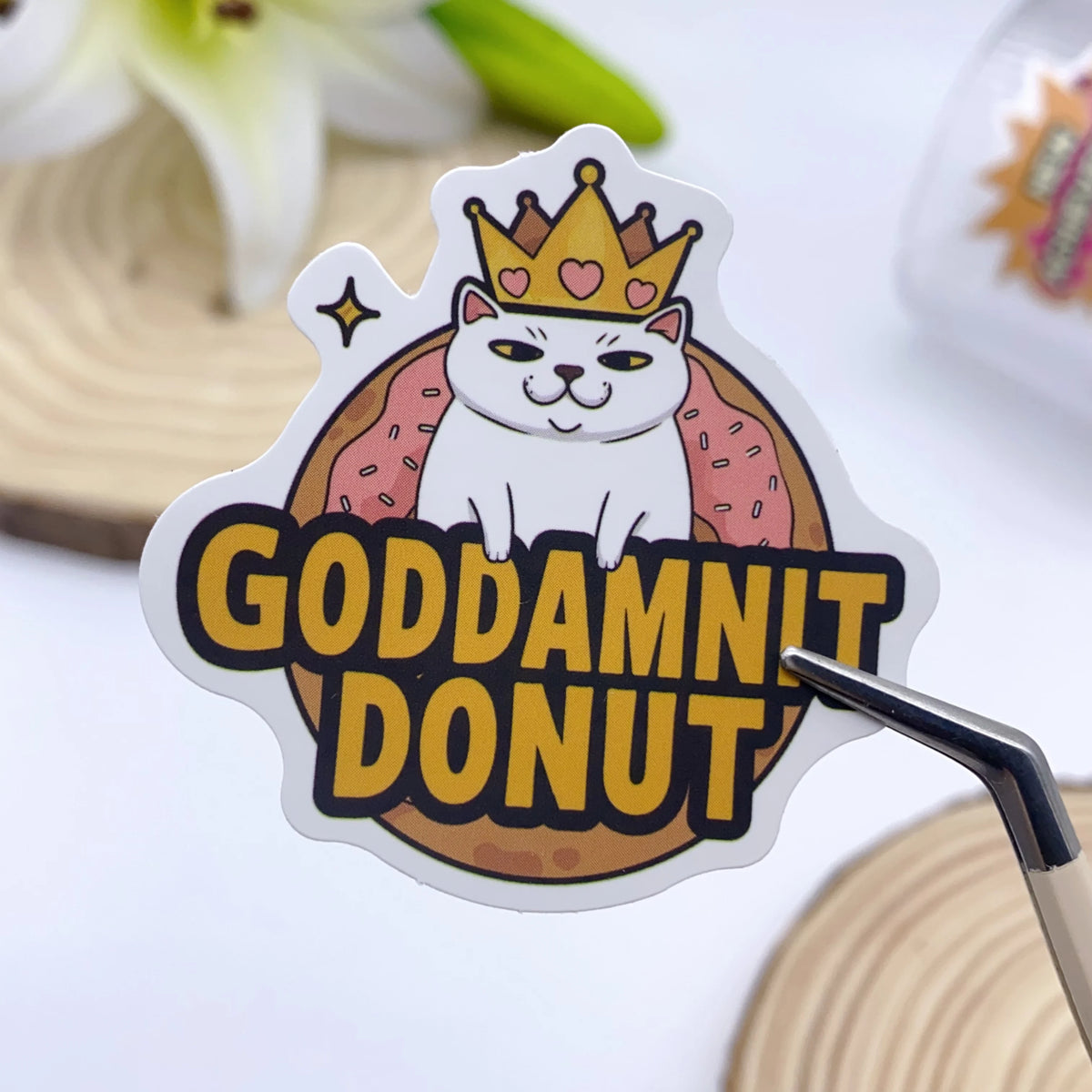 A white cat wearing a gold crown is featured on a yellow sticker with the text GODDAMNIT DONUT.