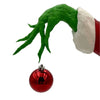 A green hand decoration is shown emerging from a red and white Santa hat, with a shiny red Christmas ornament below.
