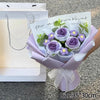 A handmade crochet flower bouquet featuring purple and yellow flowers wrapped in lilac paper.