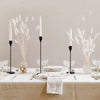 Three metal taper candle holders with white reeds arranged on a linen-covered table.