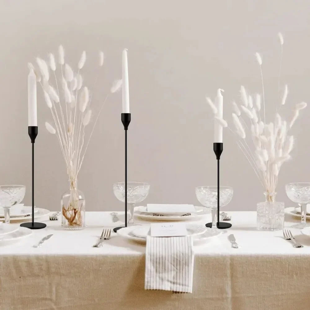 Three metal taper candle holders with white reeds arranged on a linen-covered table.