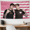 A portrait of two young men making peace signs against an American flag tapestry.